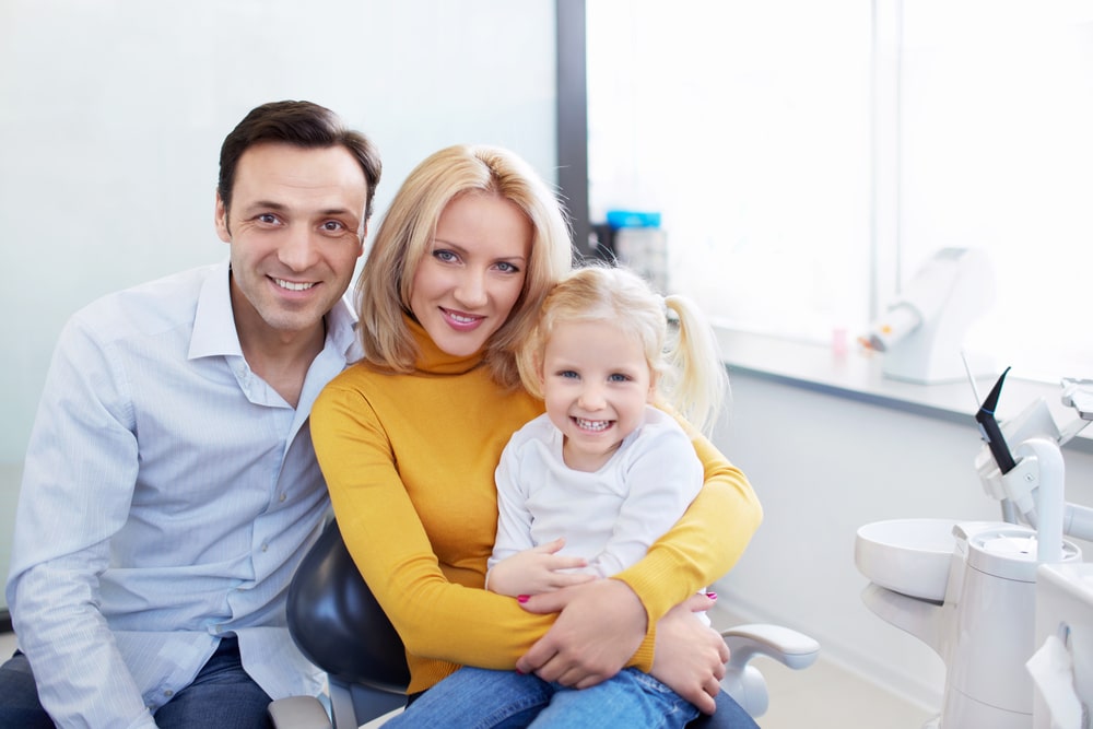 Parents and little girl smiling in dentist office